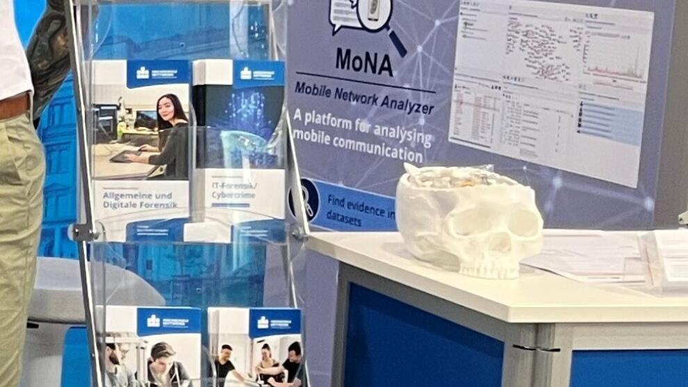 Fünf Personen stehen an einem Messestand; ein Torso trägt ein beschichtetes Shirt