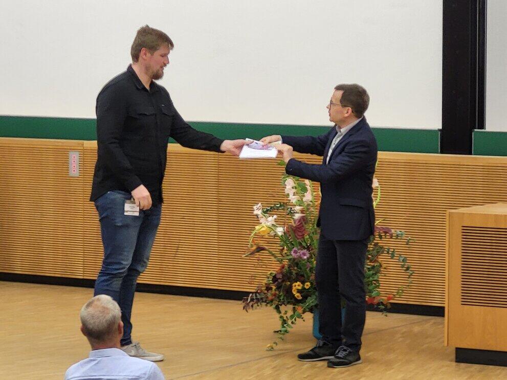 Two men shake hands; a prize is presented