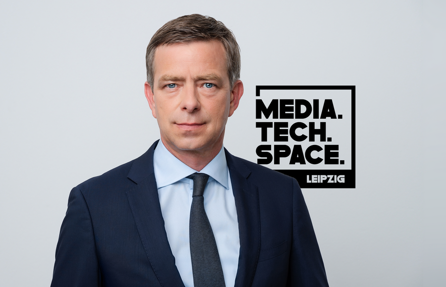 Ein Mann im Anzug mit Hemd und Krawatte guckt in die Kamera. Rechts ist das Logo des MediaTechSpace sichtbar.