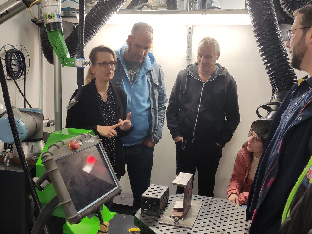 Personen stehen um einen Schweißroboter