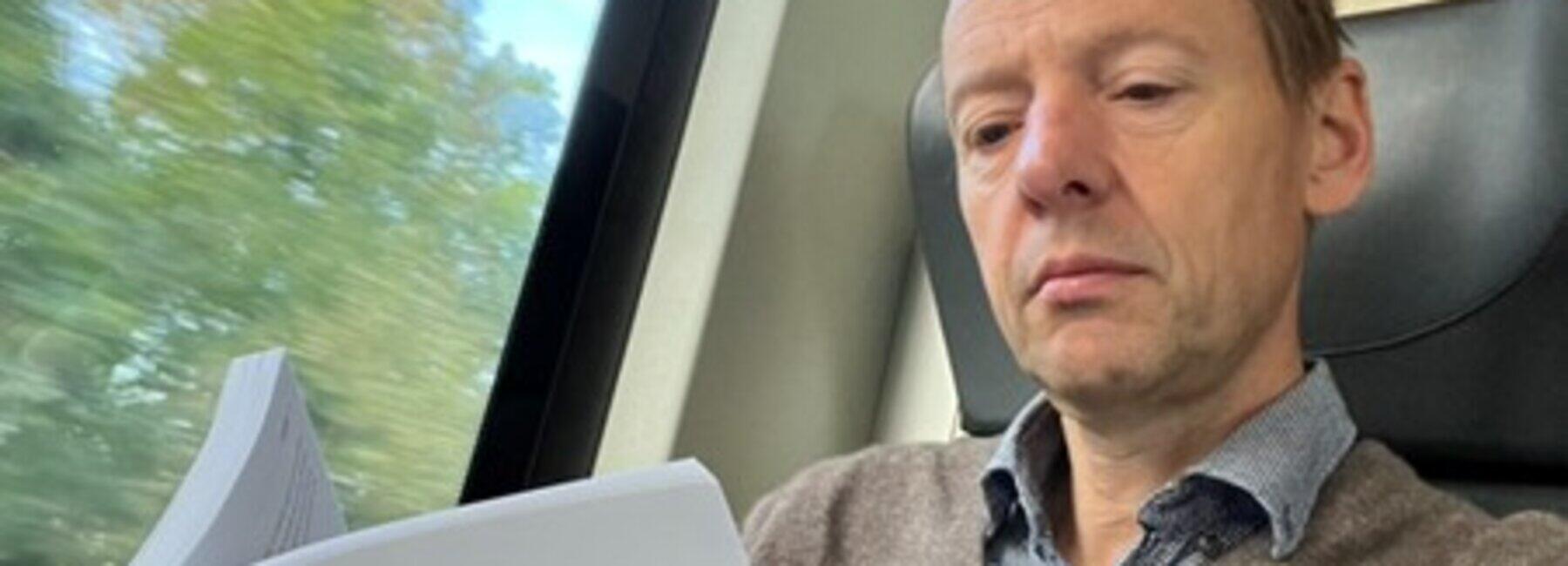 Männliche Person sitzt lesend im Zug