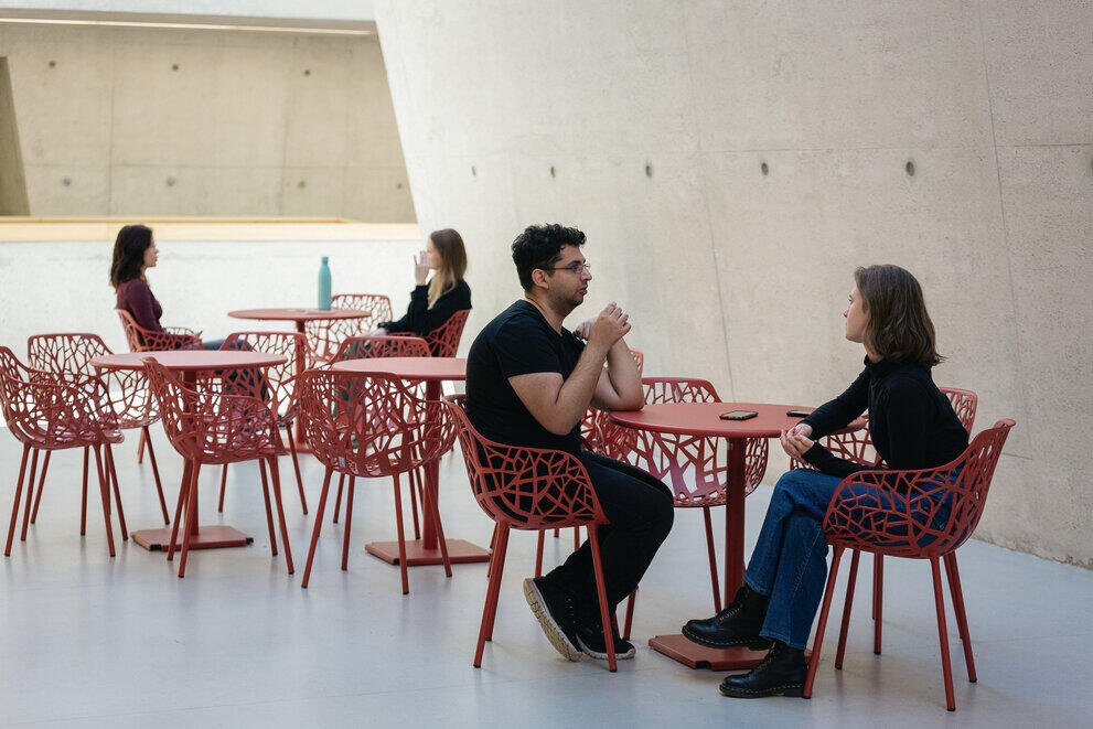 Four students are sitting at different tables, chatting.