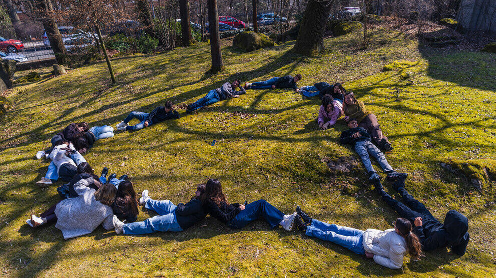Jugendliche formen auf einer Wiese liegend ein Herz