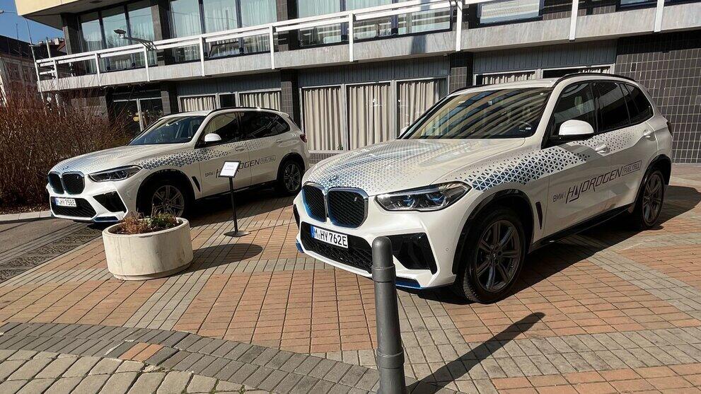 Zwei weiße BMW-Fahrzeuge vor einer Messehalle