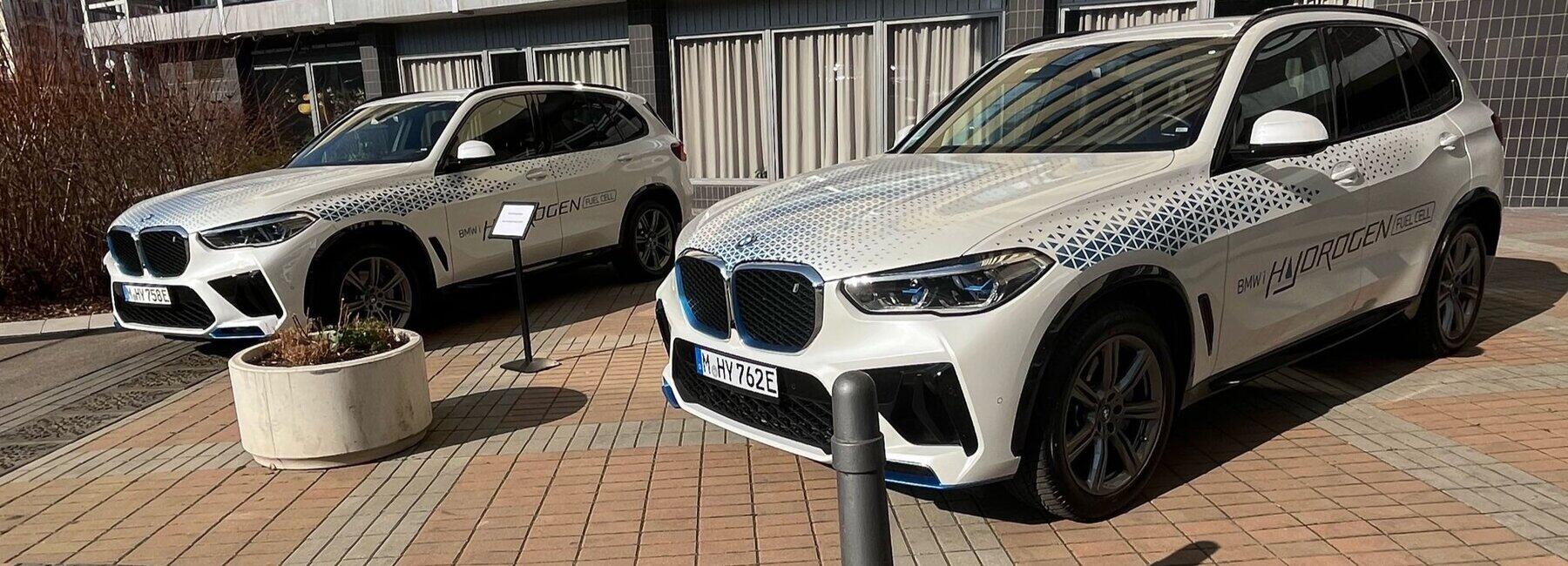 Zwei weiße BMW-Fahrzeuge vor einer Messehalle