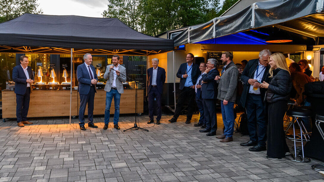 Exterior view of the Torfgrube 4 event venue. Several people; one is speaking into a microphone.