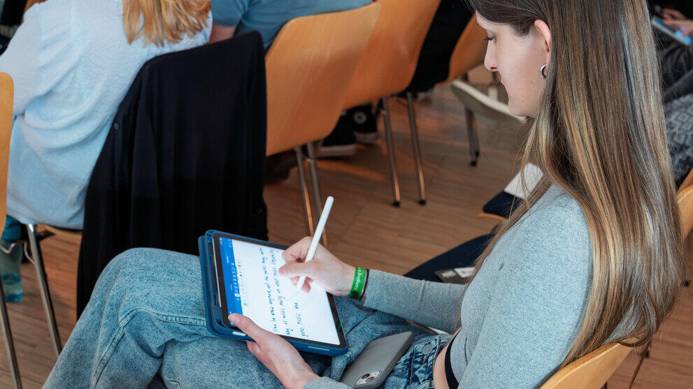 Blick über die Schulter einer Frau, die auf ihrem Tablet Notizen macht.
