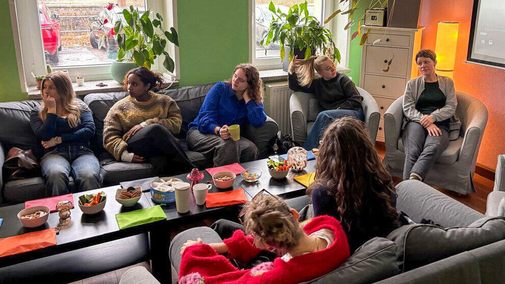 Sieben Personen auf Sofas und Sesseln  um einen Coucthtisch mit Gebäckschalen.