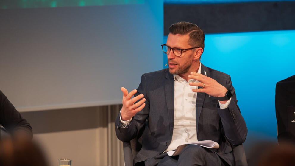 Professor Alexander Knauer sitzt auf einem Panel und gestikuliert entspannt.