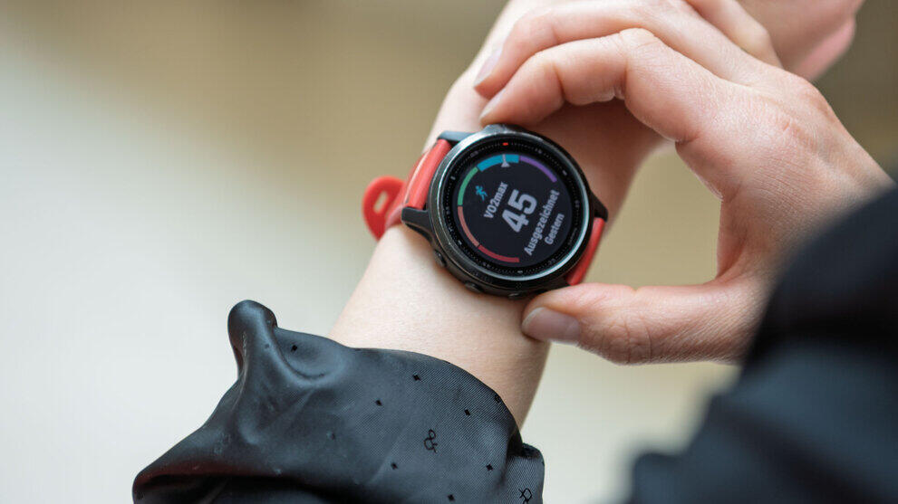 Eine Hand berührt eine runde Smartwatch am Arm. Das Display zeigt „VO2max 45. Ausgezeichnet“ an.