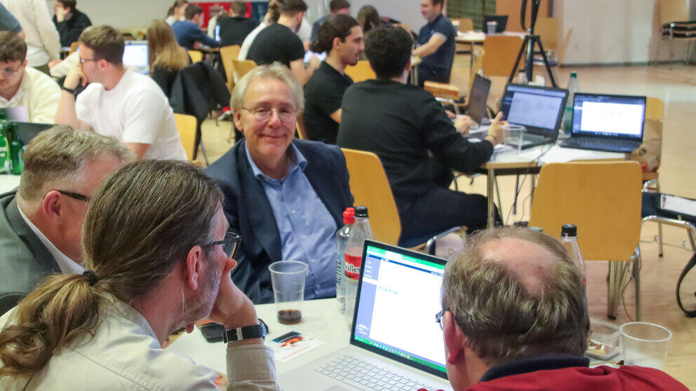 Numerous groups of people sitting at tables with laptops and drinks on them. A single man in the centre of the picture is looking at the camera.