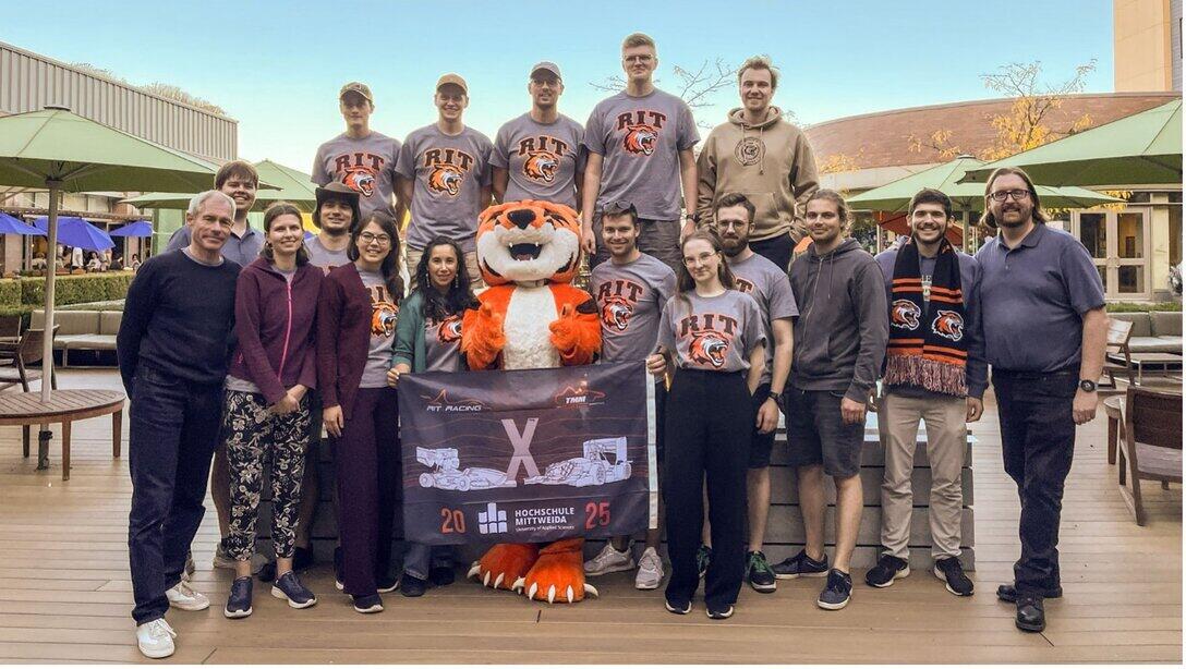 A group photo featuring a life-size tiger mascot and the participants, one of whom is wearing an RIT T-shirt.