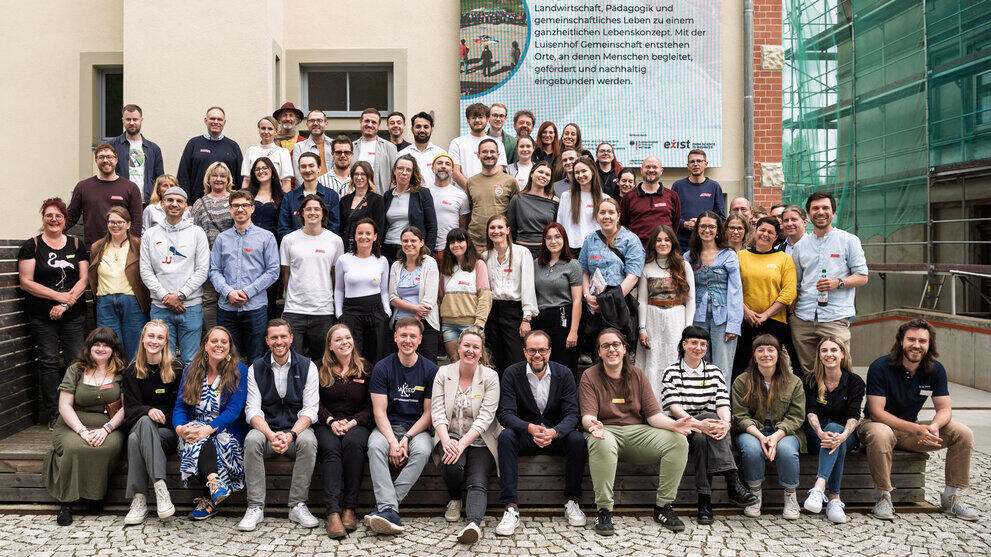 Gruppenfoto mit Personen die auf einem ansteigenden Podest vor einer Hauswand stehen.