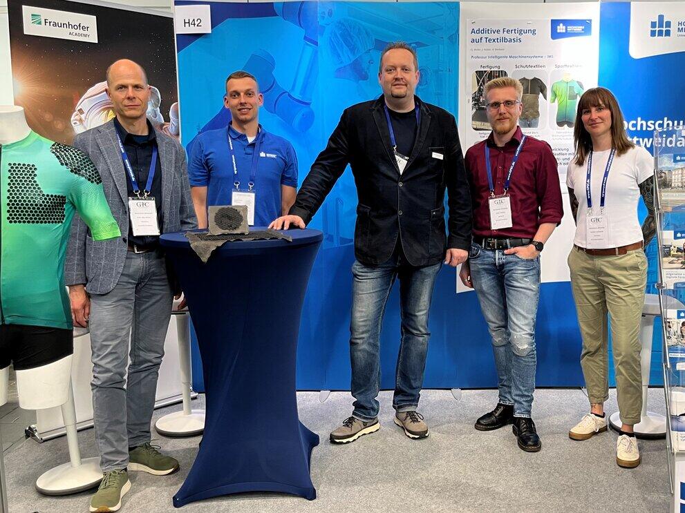 Fünf Personen stehen an einem Messestand