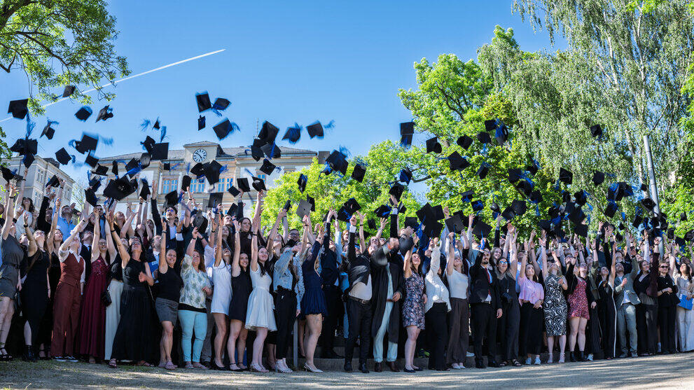 Eine große Gruppe von Studierenden wirft gleichzeitig die Graduiertenhüte in die Luft.
