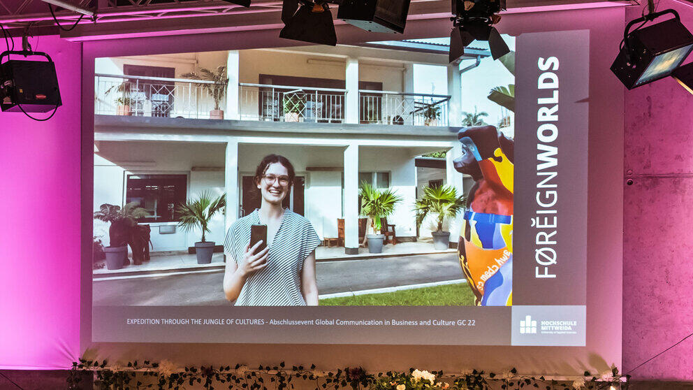 A video is shown on the screen in which a young woman is speaking towards the camera in front of a building with columns and palm trees.