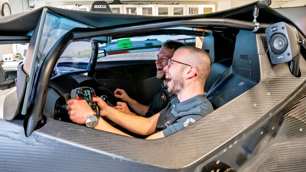 Two young men, laughing heartily, in the cockpit of the simulation platform.