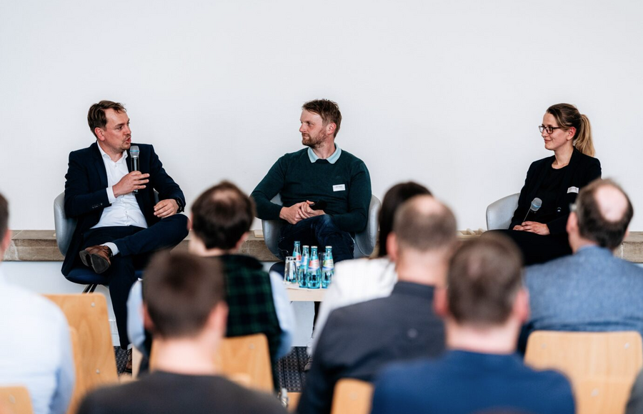 Drei Personen sitzen vor Publikum im Gespräch