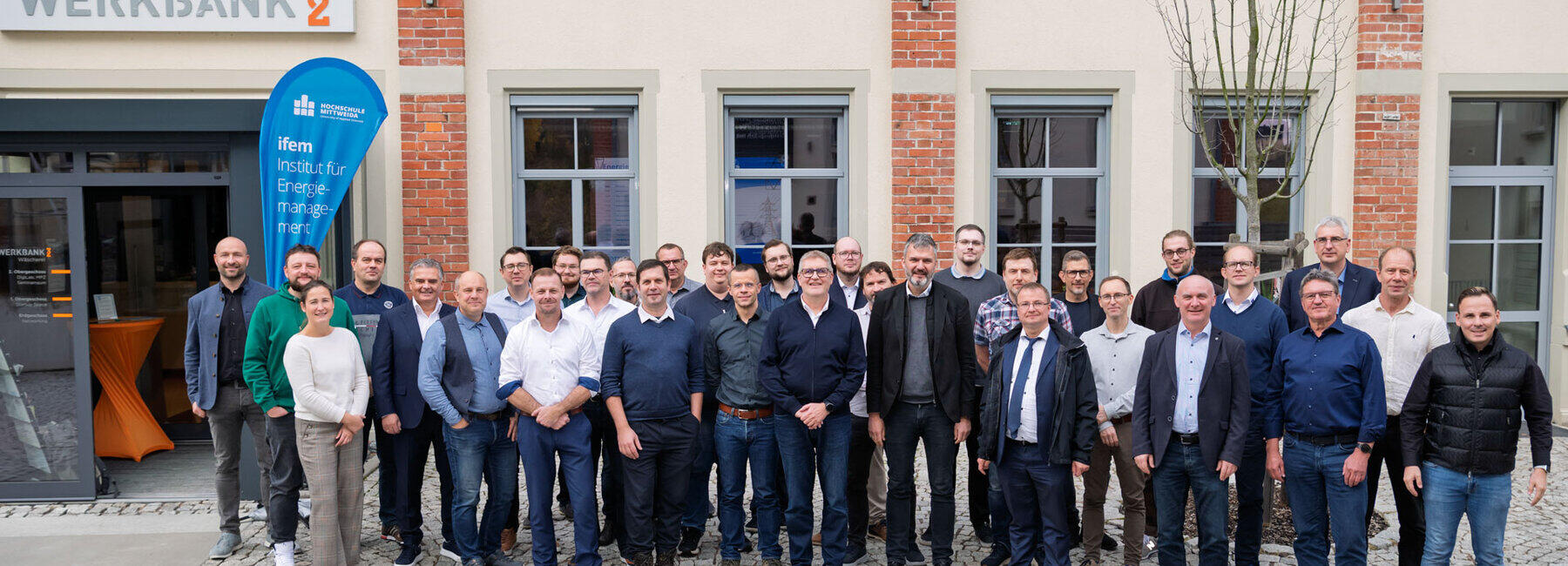 Gruppenfoto mit 32 Personen, darunter eine weibliche, vor einem Backsteingebäude mit der Aufschrift "Werkbank 32"