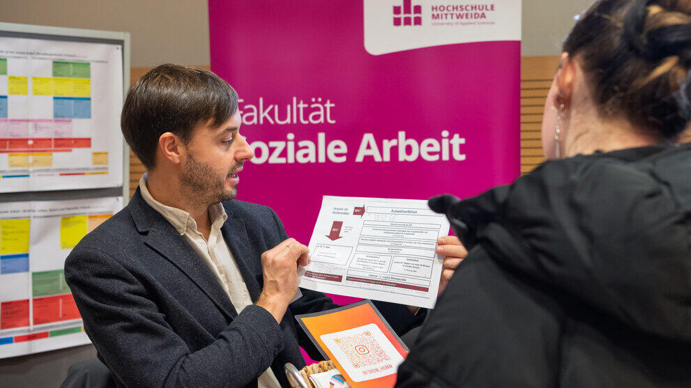 Männliche Person vor Rollup "Soziale Arbeit" zeigt ein Papier zum Thema "Auswahlverfahren".