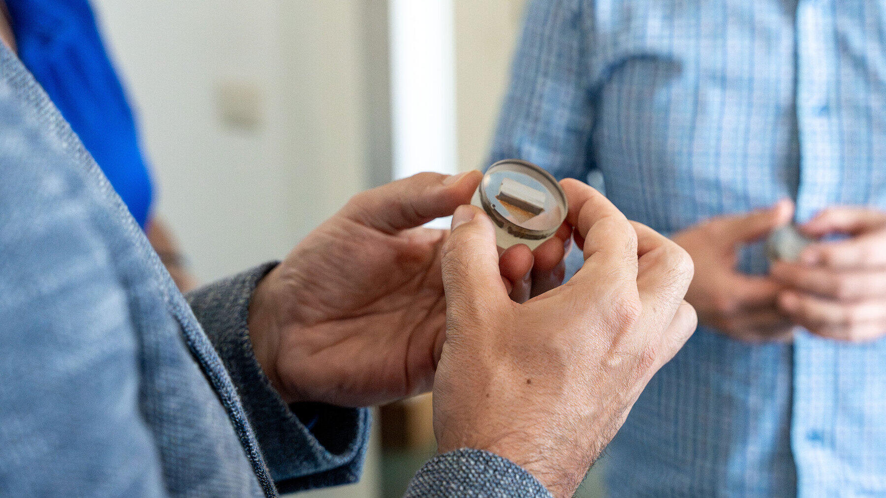Hände von zwei Personen, eine hält eine Probe in der Hand