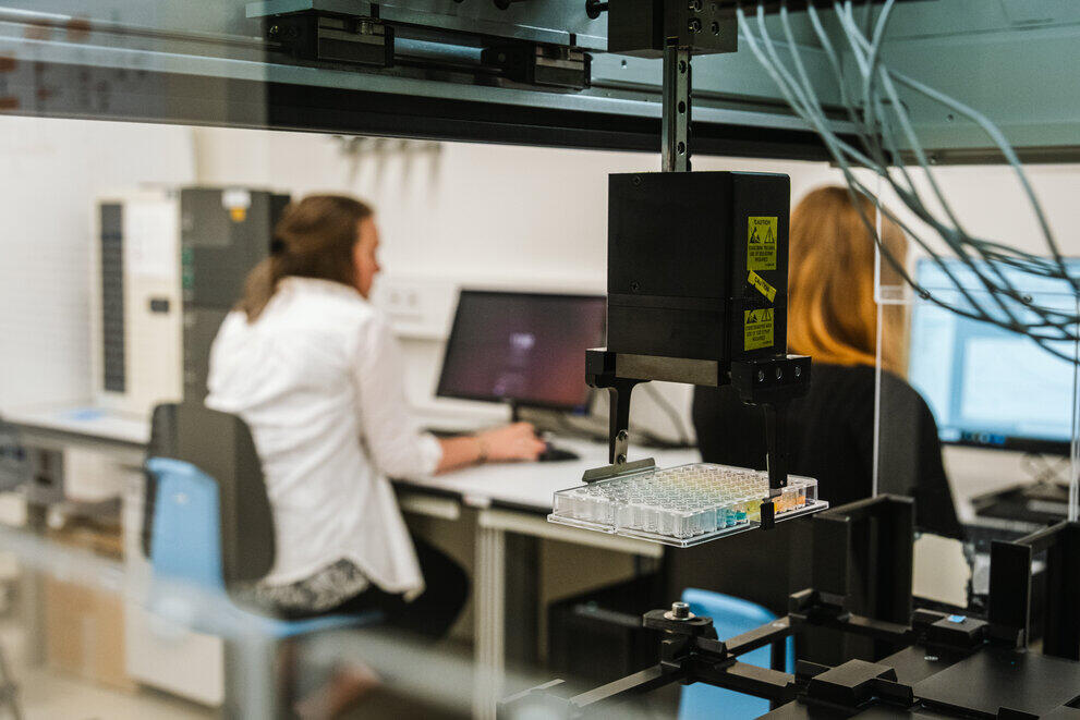 Zwei Studentinnen sitzen am PC und steuern einen Pipettierroboter.