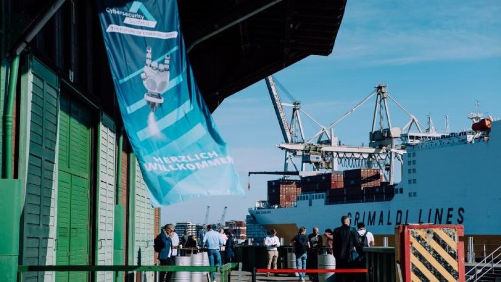 Blick auf ein Hafengebäude mit Personen und einem Containerschiff