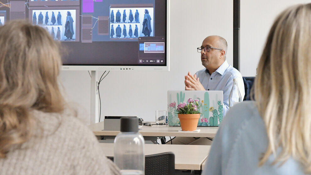 A lecturer is sitting in front of a group of students, giving a lecture.