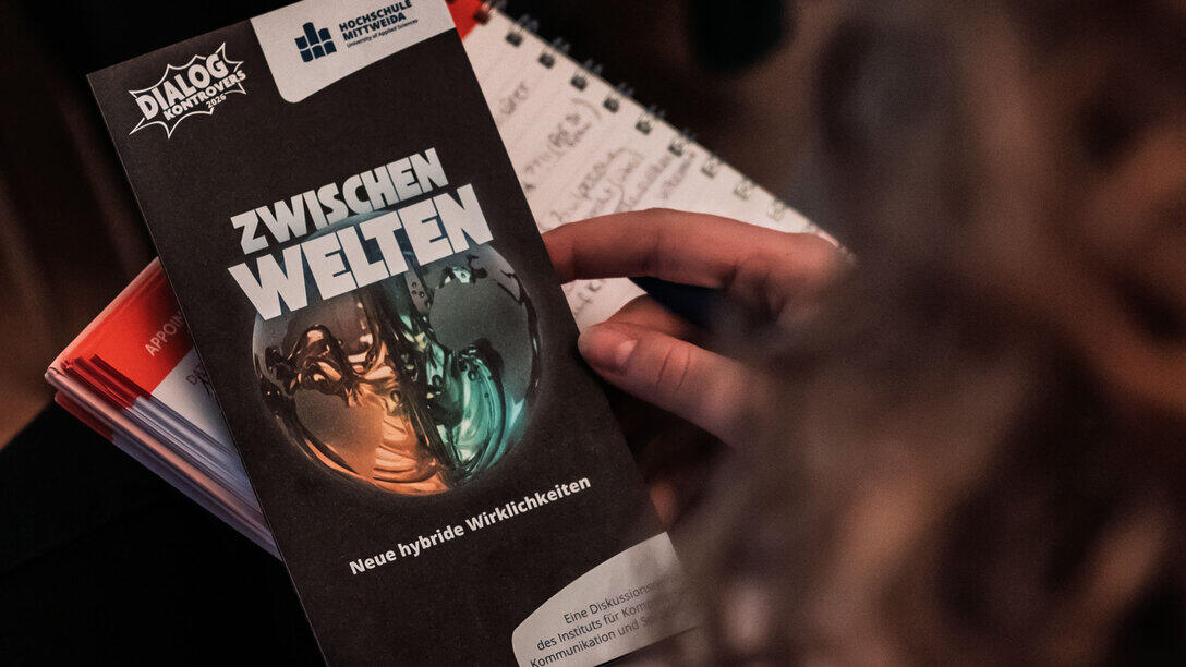 Eine Person hält den Veranstaltungsflyer in der Hand