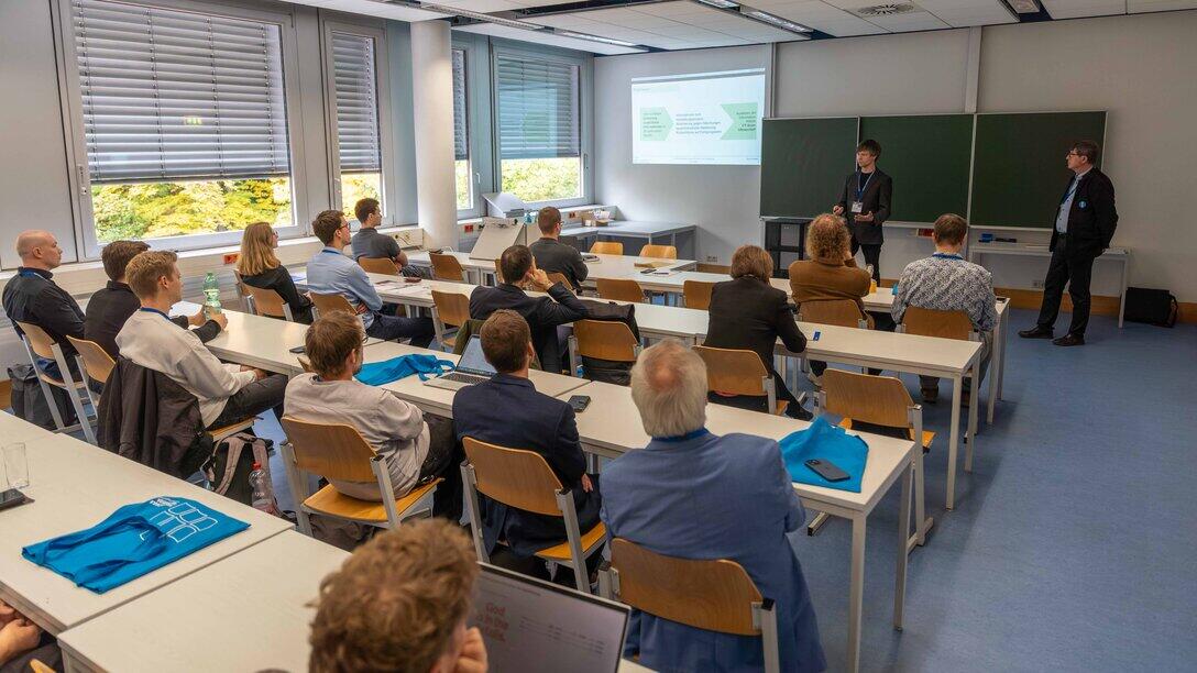 Blick in einen gefüllten Seminarraum mit zwei vortragenden Personen an der Tafelseite