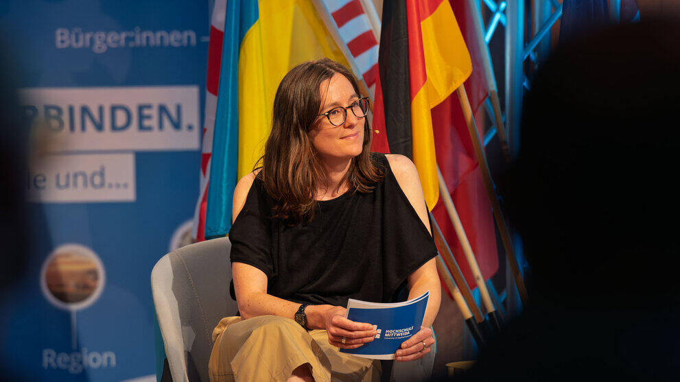 Weibliche Person mit Moderationskarten im Sessel auf dem Podium