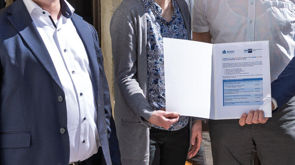 Drei männliche und eine weibliche Person halten eine Mappe in der Hand