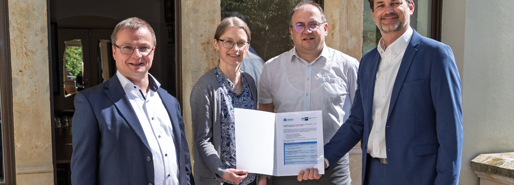 Three men and one woman are holding a folder