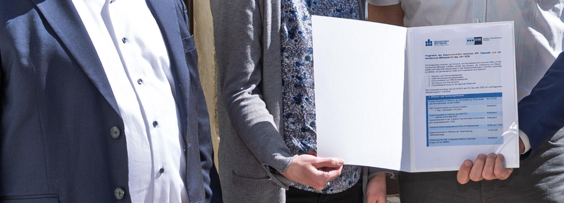 Drei männliche und eine weibliche Person halten eine Mappe in der Hand