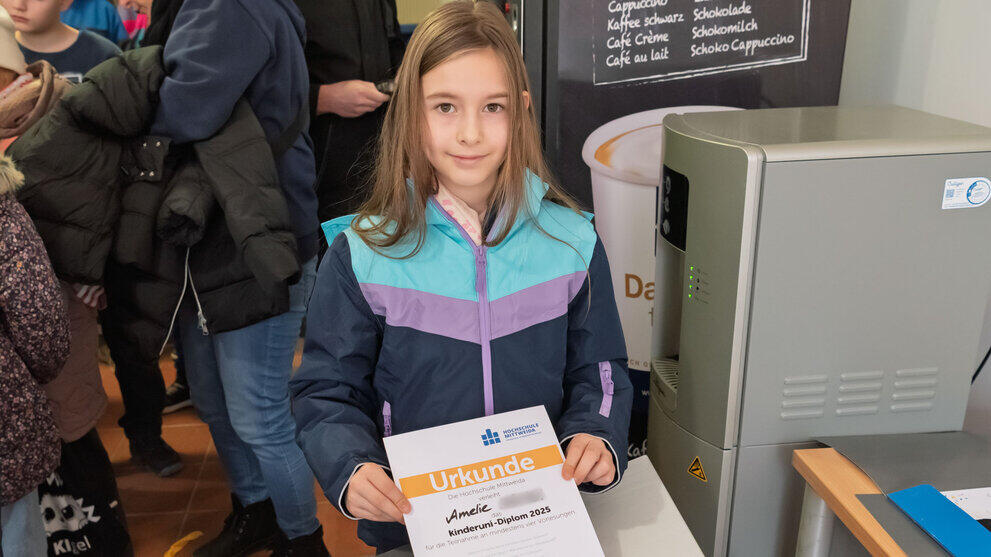Mädchen hält ihre Urkunde in die Kamera und lächelt.