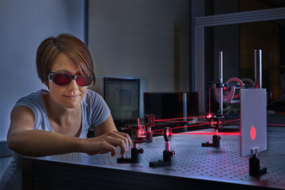 Eine Studentin mit Schutzbrille sitzt vor einem Laser-Versuchsaufbau.