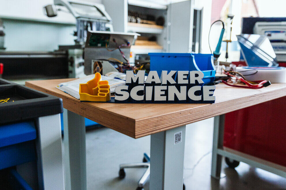 Der 3-D-gedruckte Schriftzug "Maker Science" steht zusammen mit einem Daumen aus Kunststoff auf einer Werkbank.