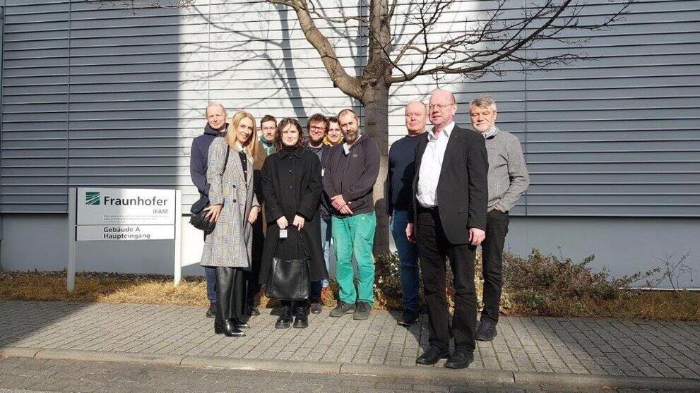Gruppe von 10 Personen steht vor einer Hauswand und neben einem Schild des Fraunhofer IFAM