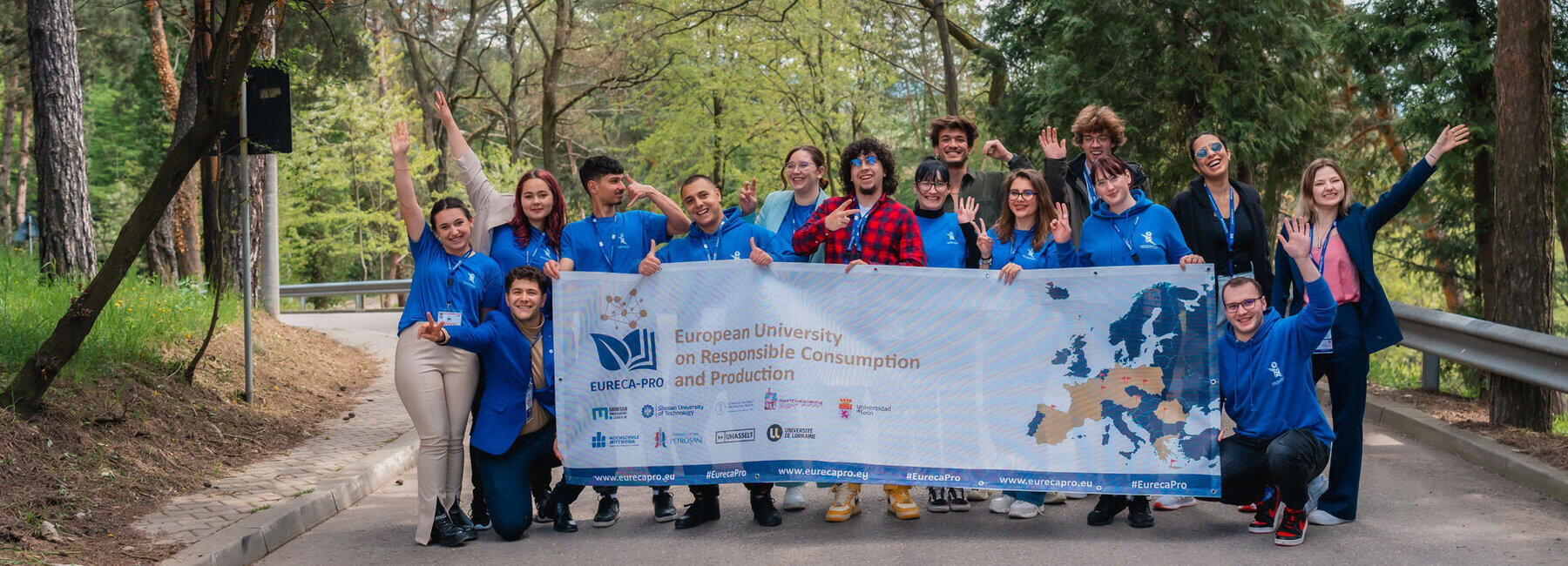In a group photograph, 15 students are holding a large mesh banner featuring the EURECA-PRO university alliance logo, facing the camera.