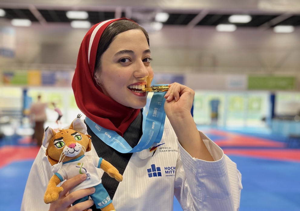 Eine Taekwondo-Kämpferin mit HSMW-Logo beißt in eine Medaille.