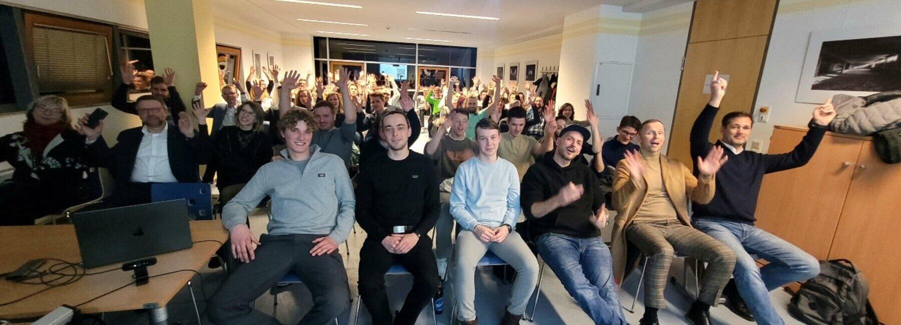 Menschen sitzen auf Stühlen und schauen in die Kamera
