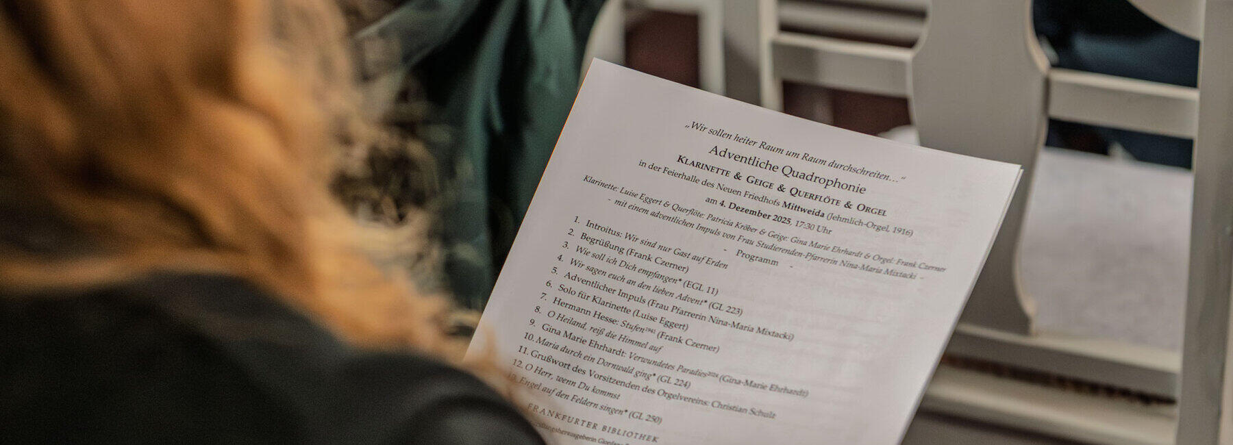 Blick über die Schulter einer sitzenden Person, die ein Blatt mit der Programmabfolge in der Hand hält.