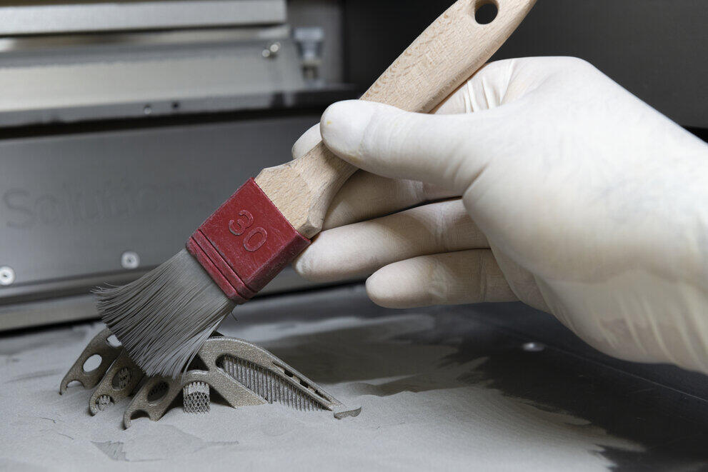 Eine Hand hält einen Pinsel und und wischt über ein 3D-gedrucktes Bauteil.