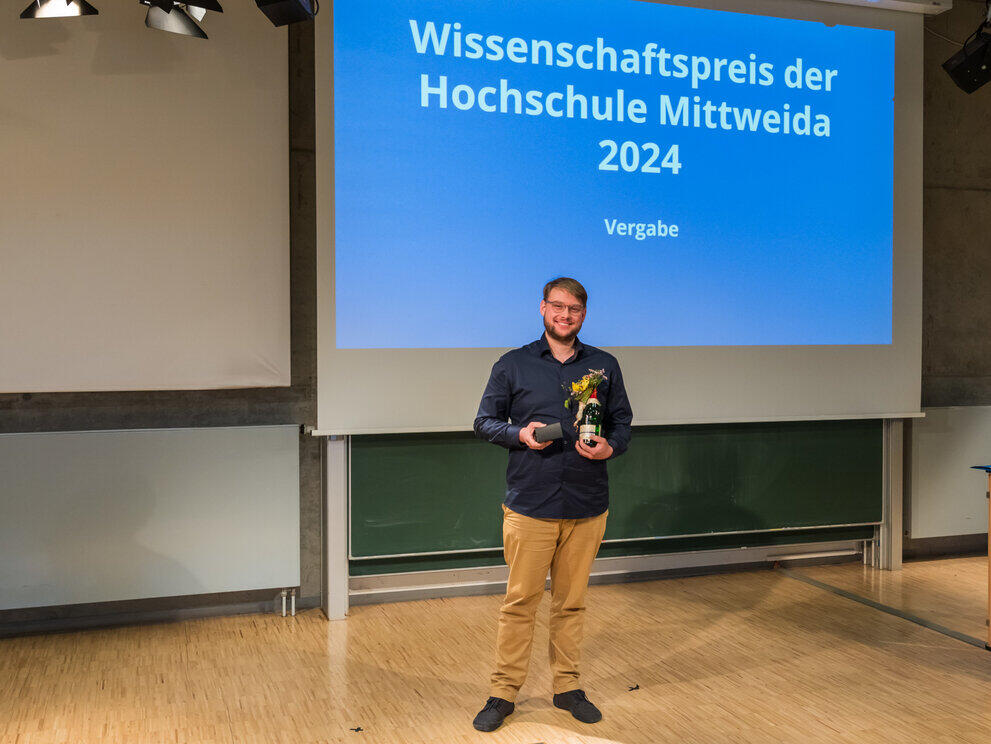 A man is standing in front of a noticeboard, holding a prize in his hand
