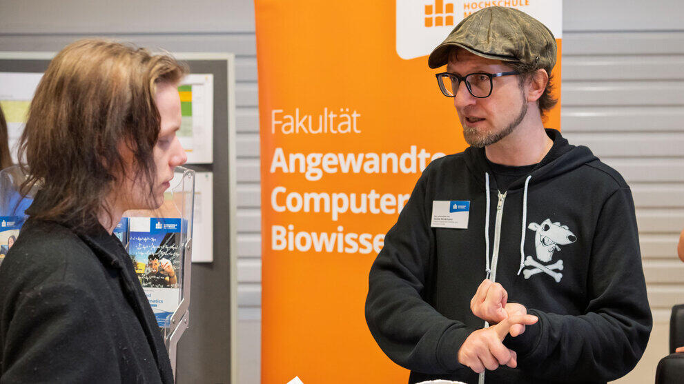 Two men in conversation in front of the roll-up banner ‘Faculty Applied Computer Sciences and Biosciences’.