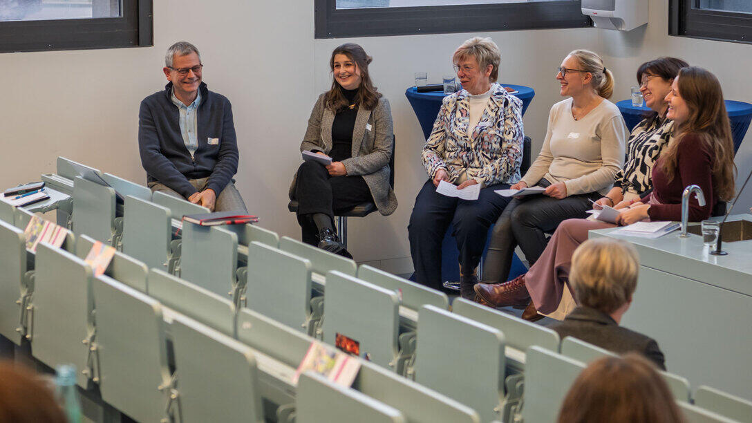 One man and five women sitting on stools at the back of the lecture theatre.