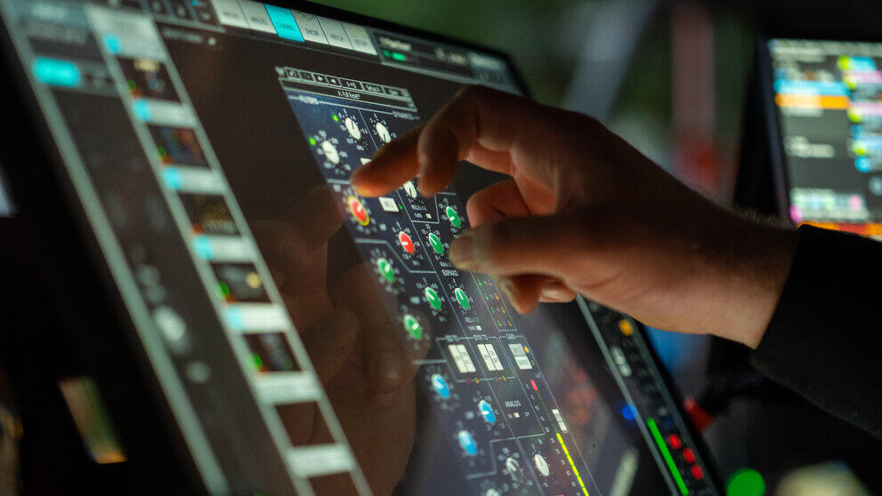 Eine Hand tippt auf ein Display und justiert einen Regler bei einem digitalen Mischpult.