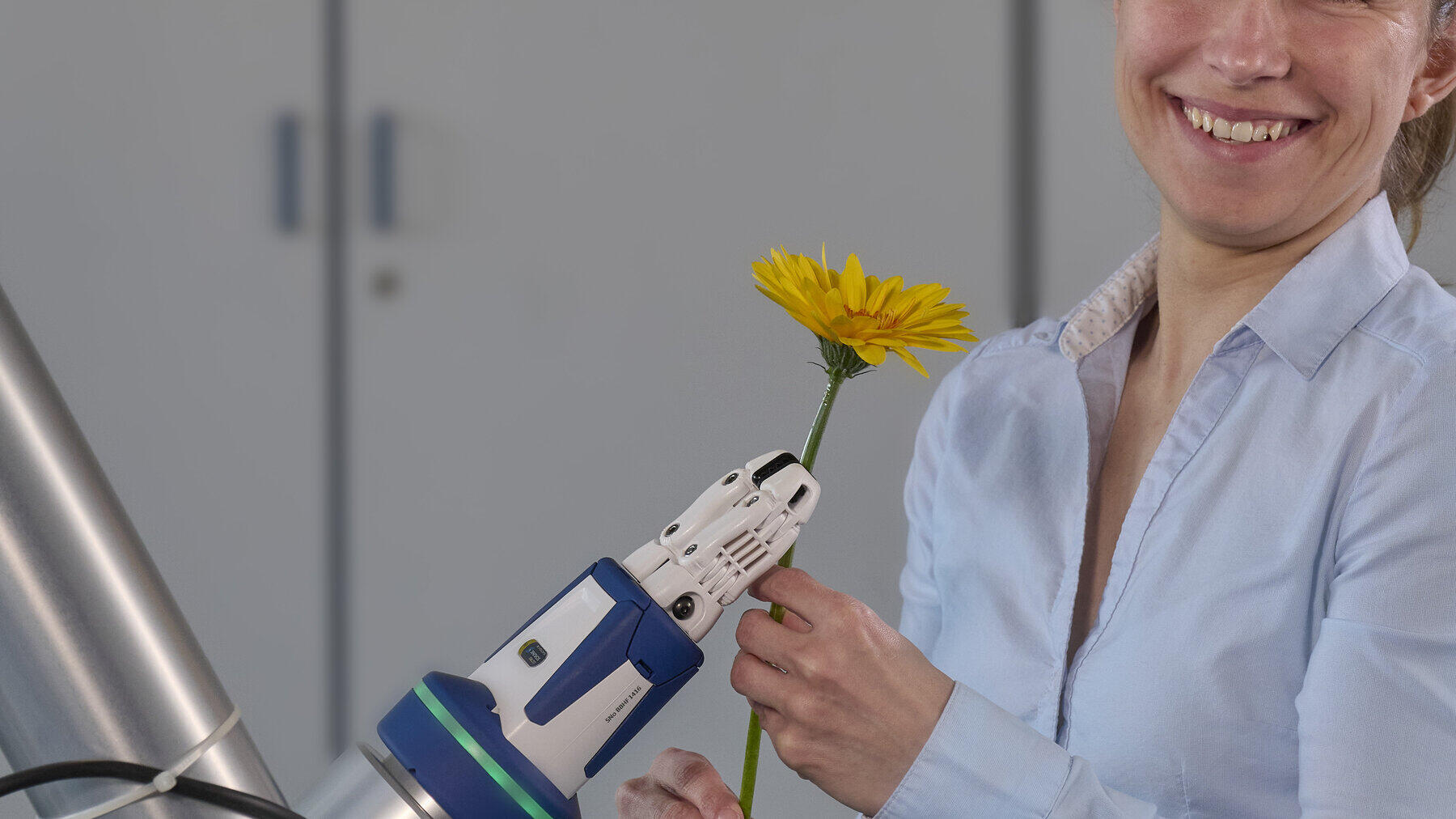 eine Person steht vor einem Roboterarm der eine Blume hält