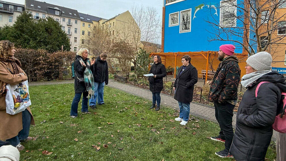 Gruppe von sieben Personen auf einer Wiese vor einem Gebäude im Gespräch