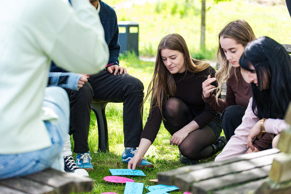 Several students are kneeling on a lawn and placing labelled pieces of paper on the ground whilst working in a group.